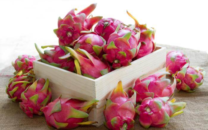 Pitaya-fruta-exótica-e-de-sabor-suave-proveniente-dos-generos-de-cactos-Hylocereus-e-Selenicereus Pitaya em lote, dentro e ao redor de caixote de madeira.