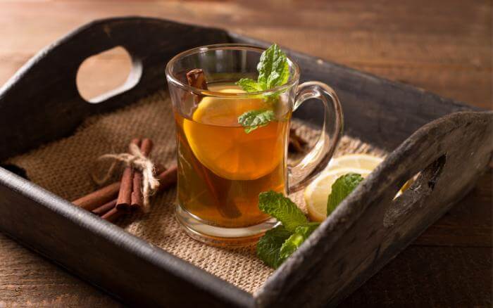 Chá de ervas em xícara, sobre bandeja de madeira.